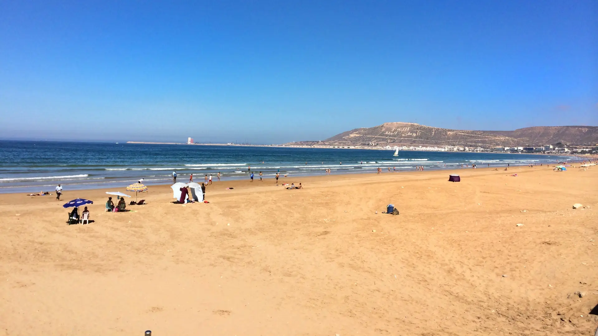 Wide sandy beach at Agadir with blue Atlantic water and the Kasbah hill in the distance