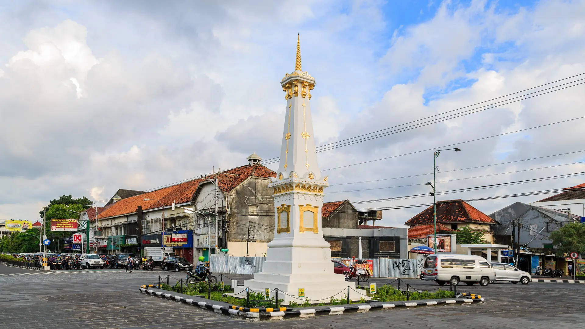White and gold Tugu monument in Yogyakarta, shown as a wider city scene