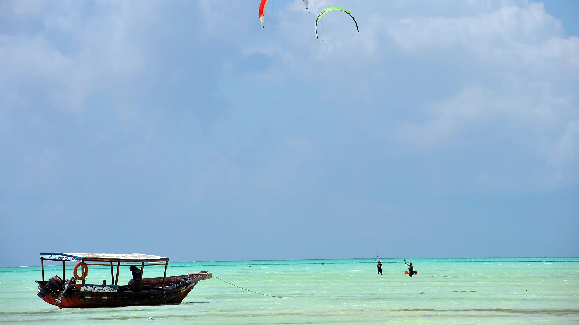 Colorful kites above Paje’s turquoise lagoon and a wooden boat
