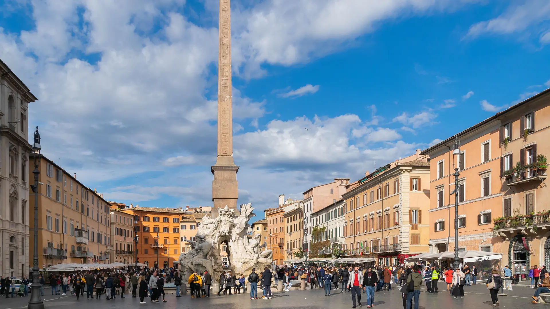 sunlit Piazza Navona with its obelisk fountain, café terraces and crowds in Rome's historic centre