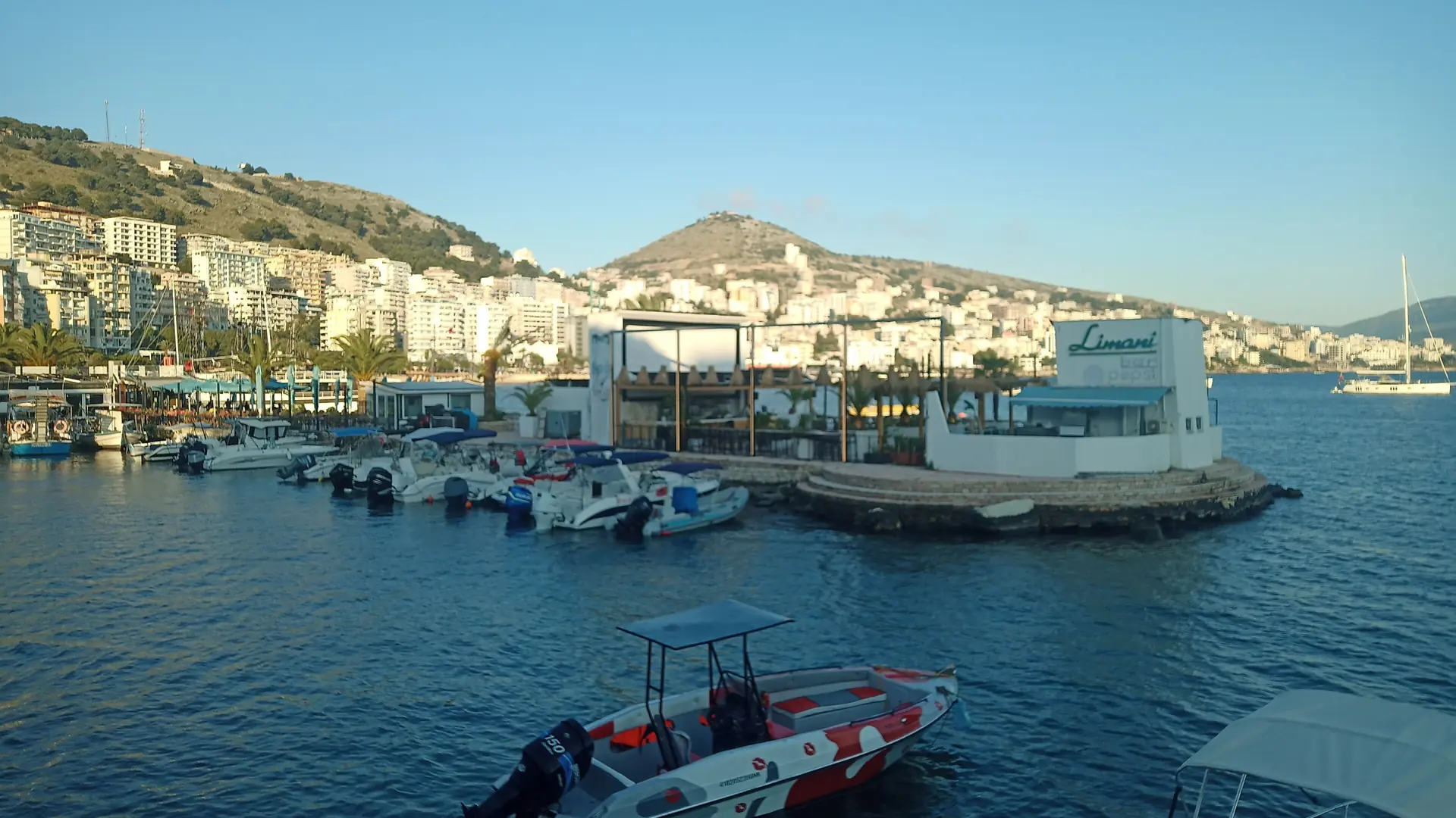 Small boats in Sarandë's central harbour below the hillside town on a sunny day