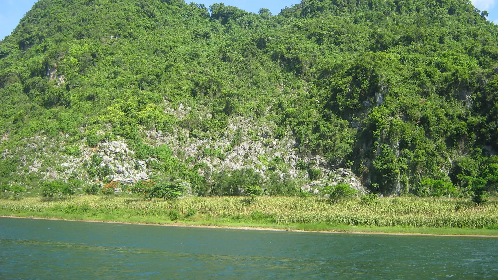 Sunlit limestone mountains, green fields and water in Phong Nha-Ke Bang National Park