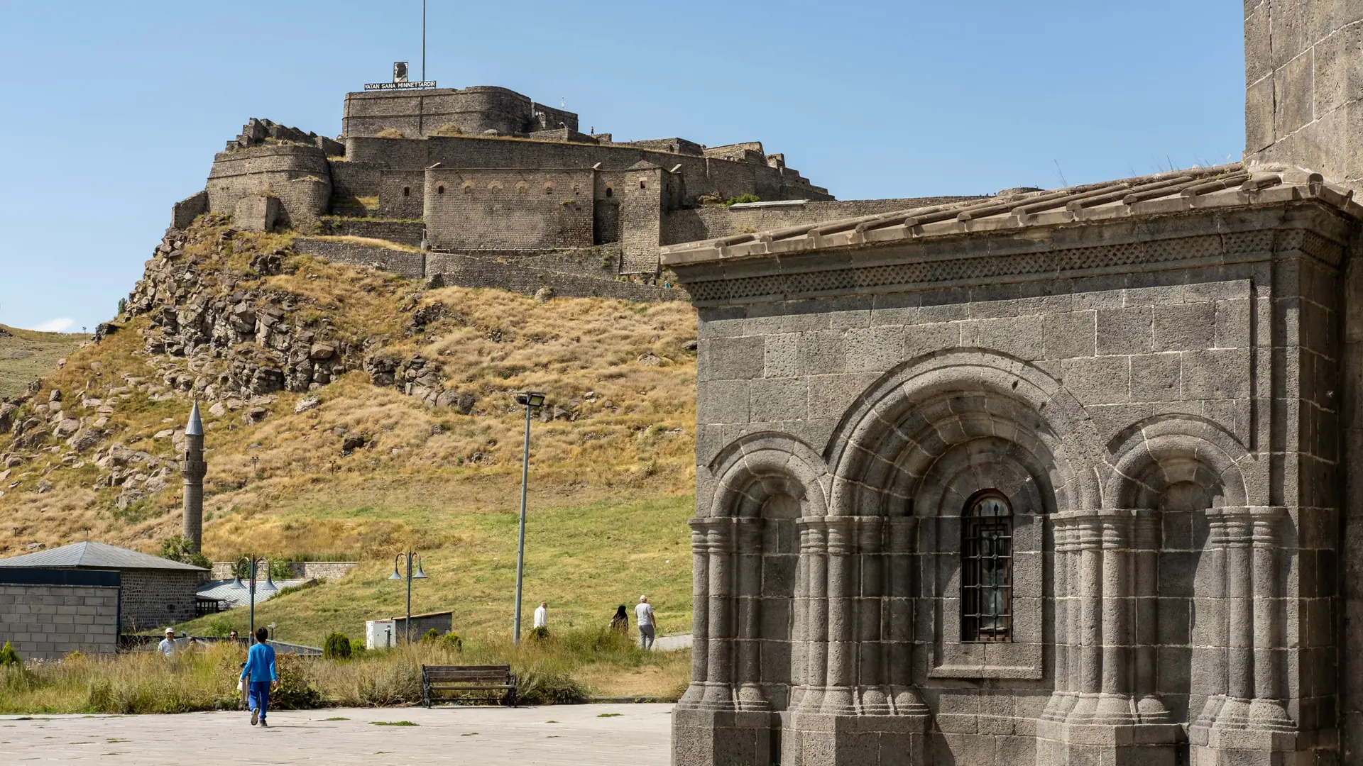 Kümbet Mosque stone arches with Kars Castle on the sunlit hill behind