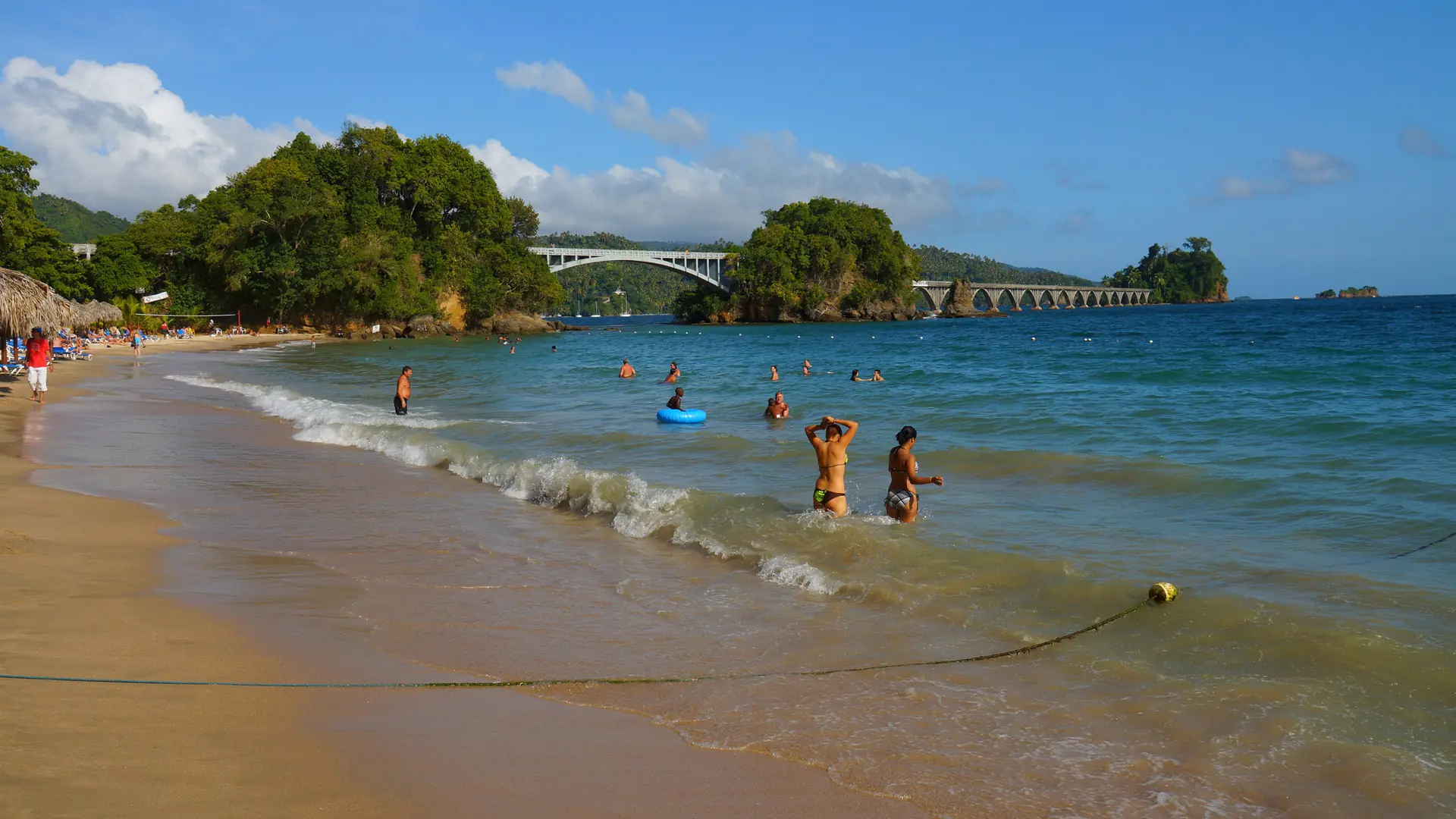 Sunny Samaná Bay beach near Cayacoa with people in shallow water and footbridge
