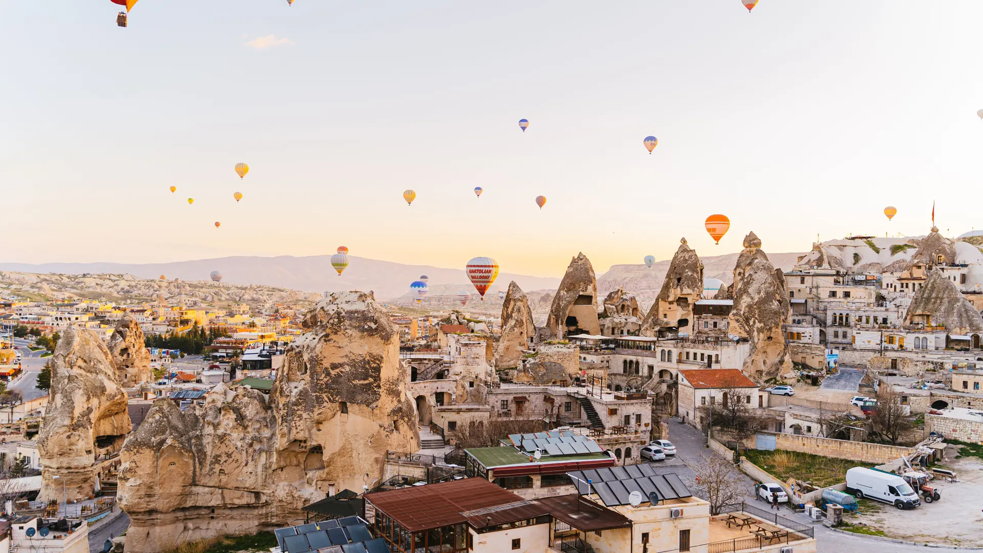 Göreme cave houses and fairy chimneys glowing beneath sunrise balloons