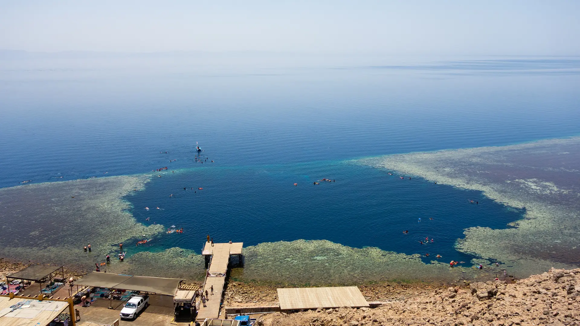 The Blue Hole north of Dahab in daylight, with its circular reef opening, swimmers and wooden shore entry.