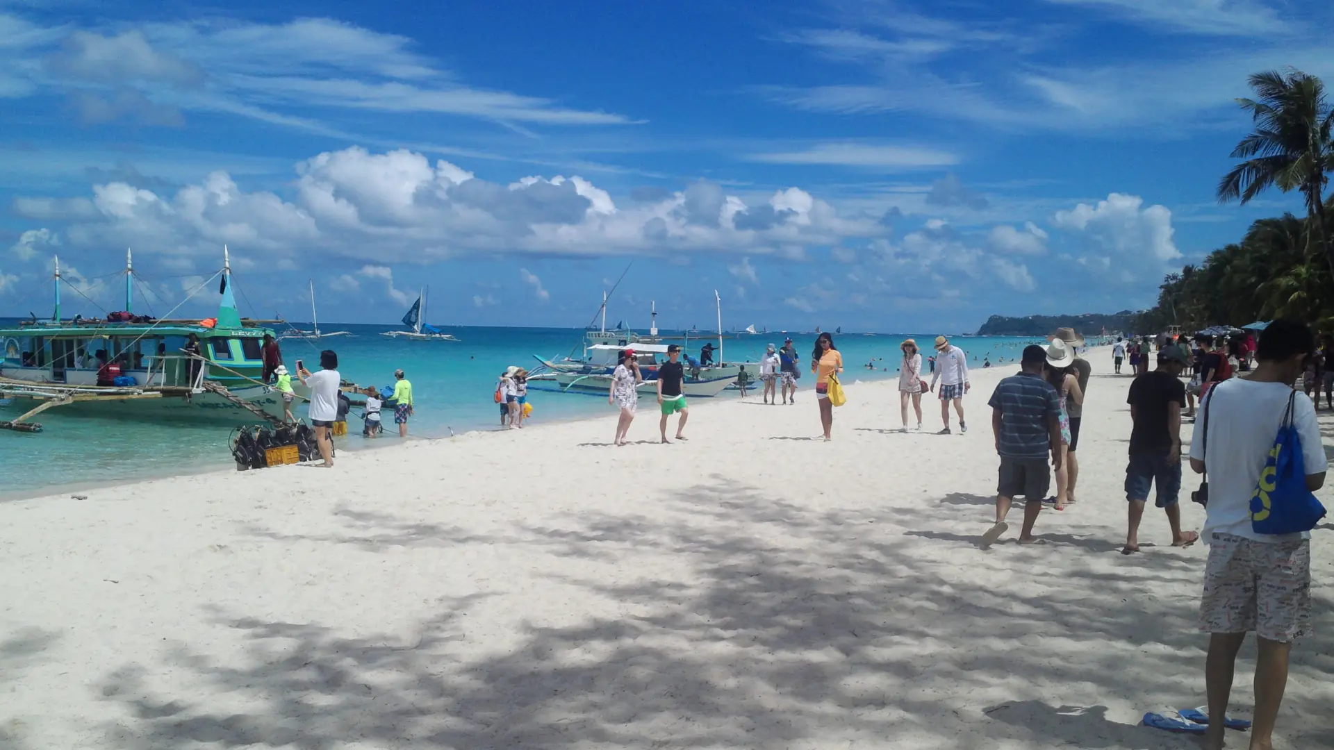 Visitors and outrigger boats on Boracay’s White Beach in bright daylight