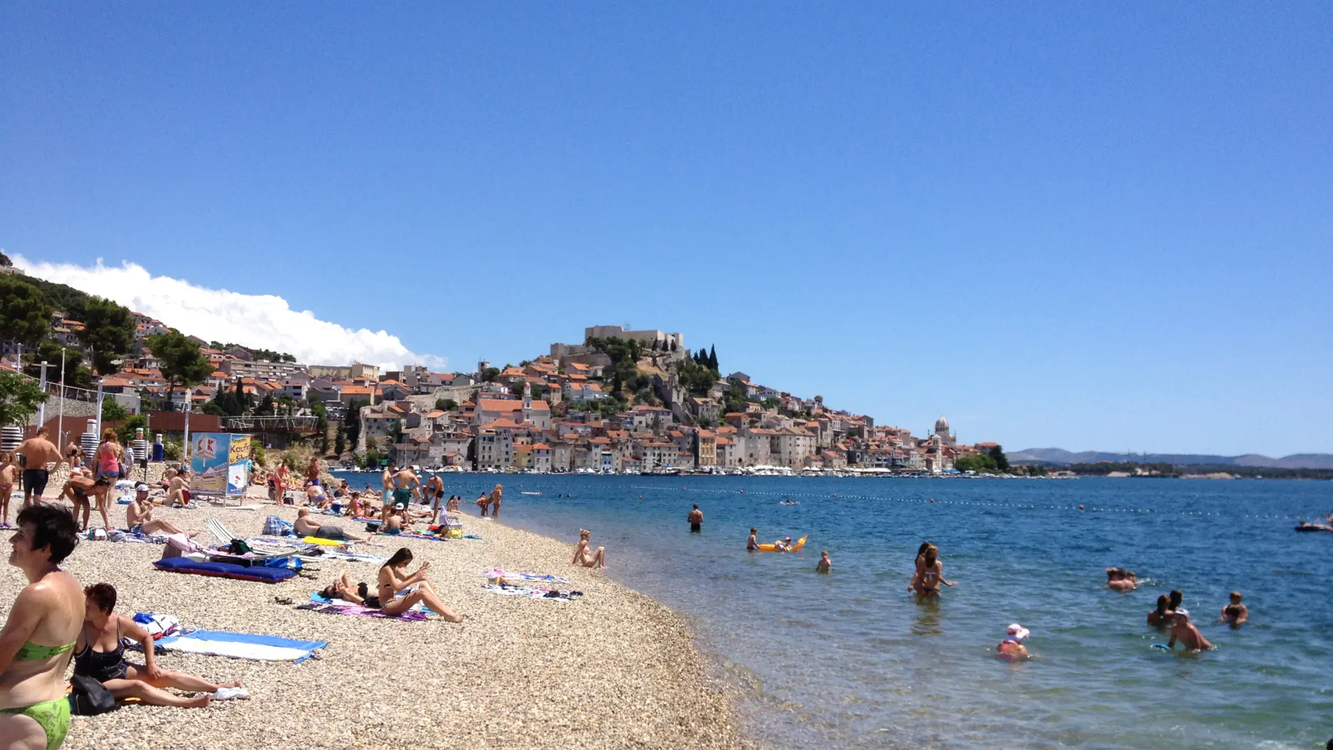 Swimmers at Banj’s pebble beach with Šibenik’s old town across the bay